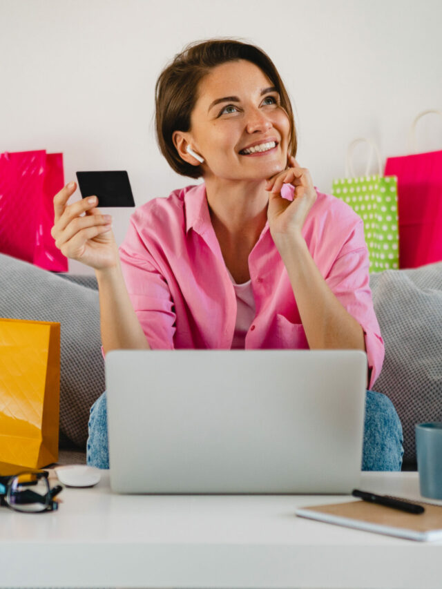 cropped-happy-smiling-woman-pink-shirt-sofa-home-among-colorful-shopping-bags-holding-credit-card-paying-online-laptop-scaled-1.jpg